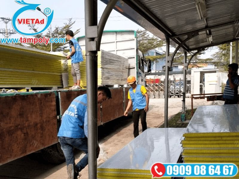 Công nhân vận chuyển tấm panel cách nhiệt từ xe tải tại công trường, sử dụng đồng phục và dụng cụ hỗ trợ