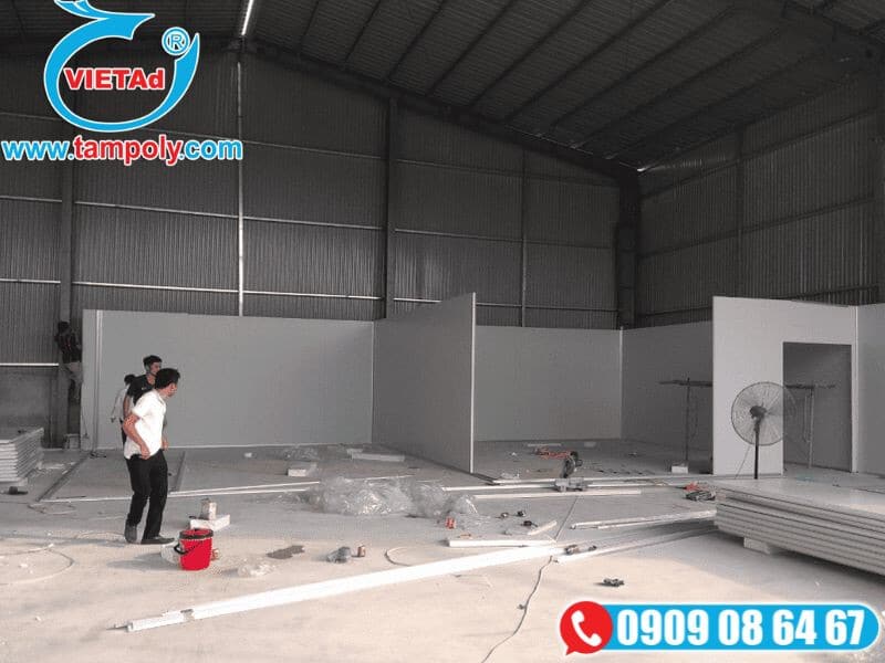 Công nhân thi công tấm panel cách nhiệt trong không gian lớn, với dụng cụ và vật liệu như xô sơn và tấm panel xếp gọn