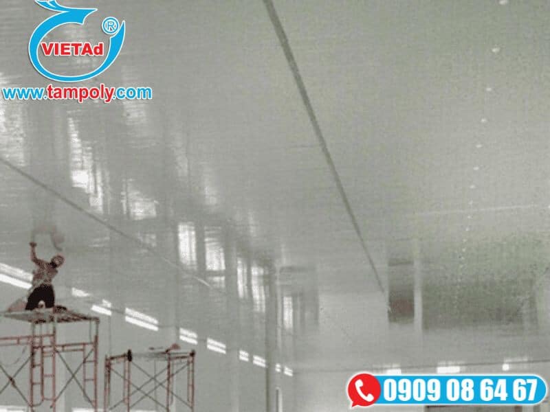Công nhân thi công trần panel cách nhiệt trong không gian lớn, sử dụng giàn giáo và dụng cụ chuyên dụng