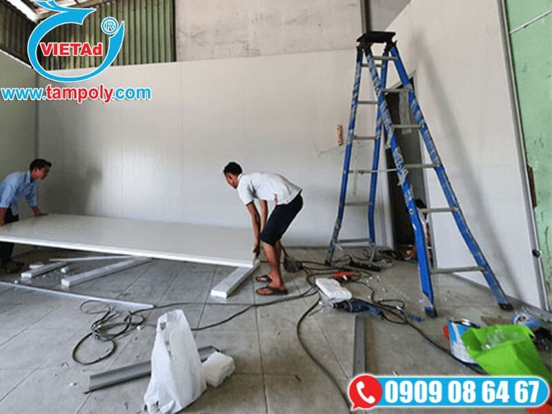 Công nhân lắp đặt tấm panel cách nhiệt tại công trình với thang và dụng cụ hỗ trợ.