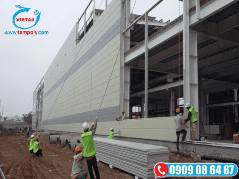 Công nhân thi công nâng lắp tấm panel cách nhiệt bên ngoài nhà xưởng bằng khung thép
